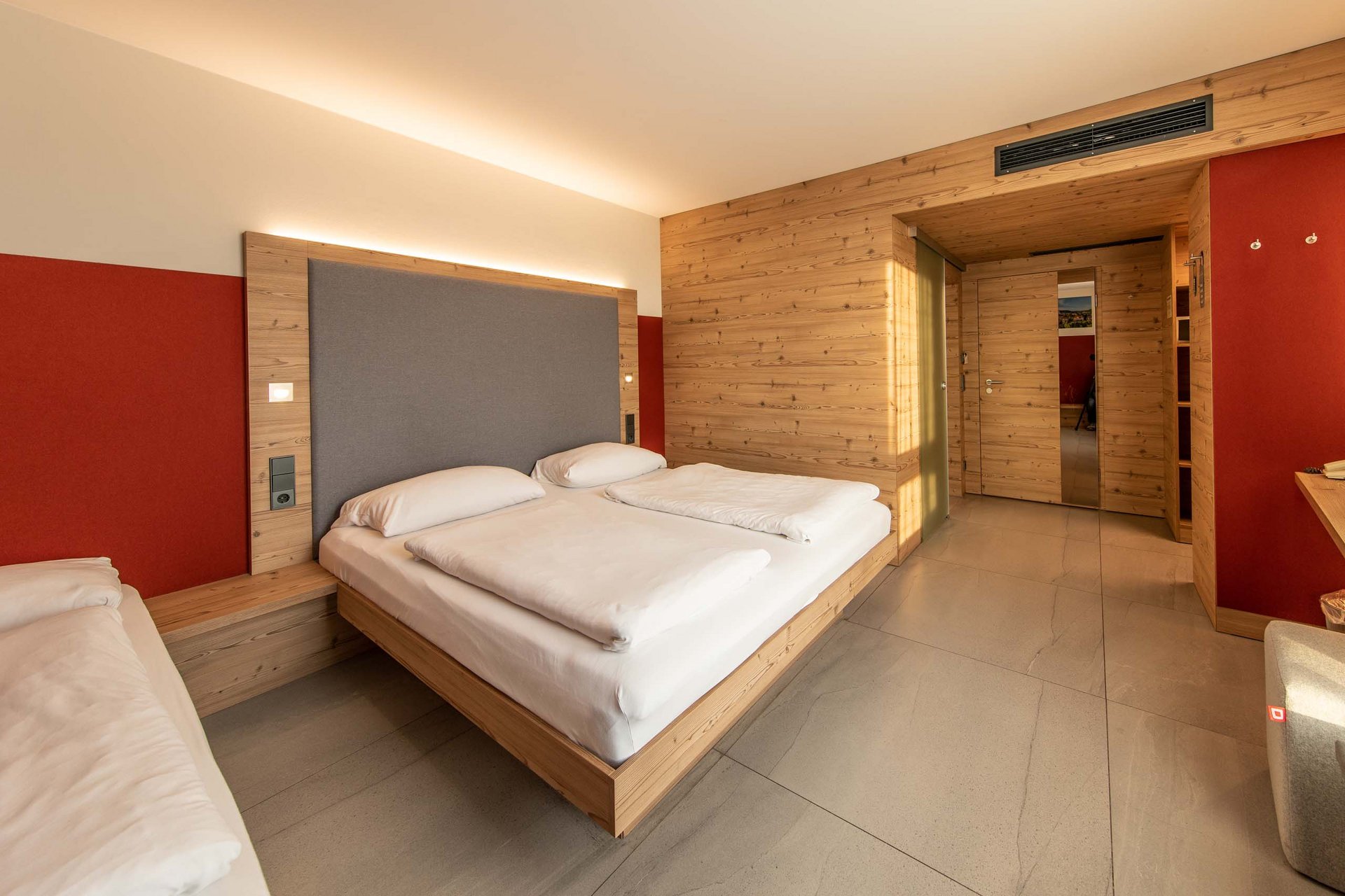 Dreibettzimmer Modernes Hotelzimmer mit Holzvertäfelung, Doppelbett und roter Wand