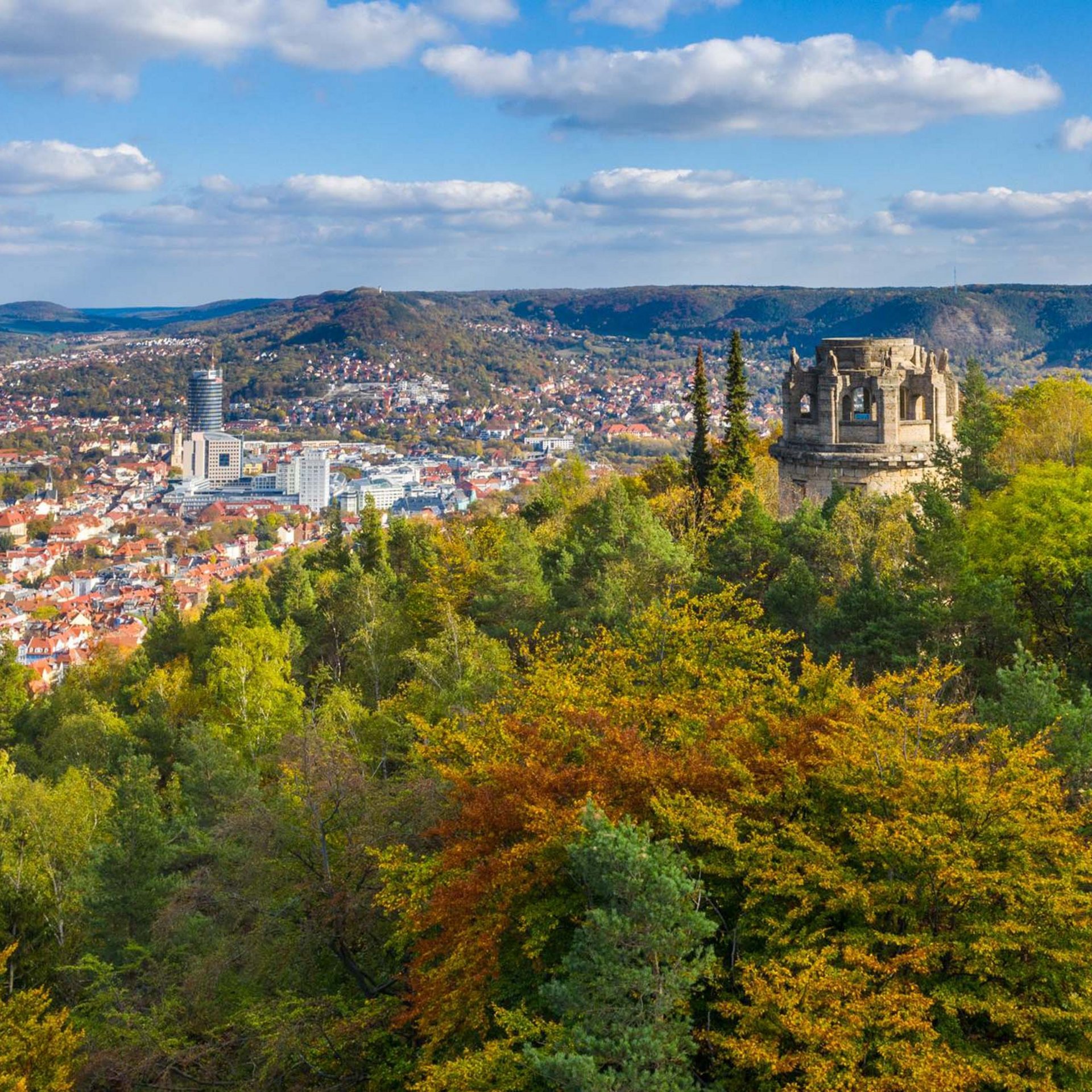 Sehenswürdigkeiten in und um Jena Blick auf eine Stadt mit herbstlichen Bäumen und einem historischen Turm auf einem Hügel