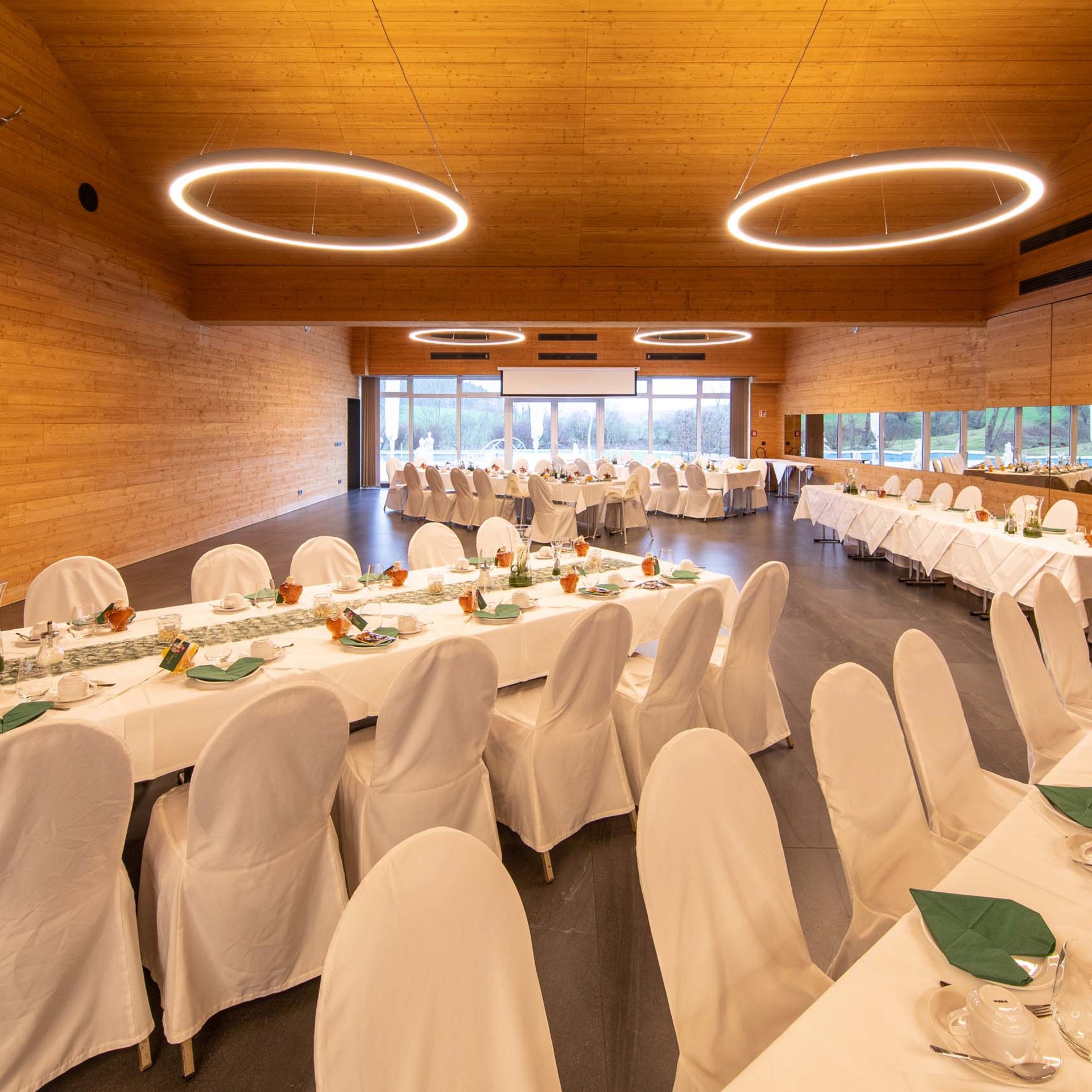 Das Event- und Tagungshotel in Jena Festlich gedeckte Tische in einem großen, modernen Veranstaltungsraum mit Holzverkleidung