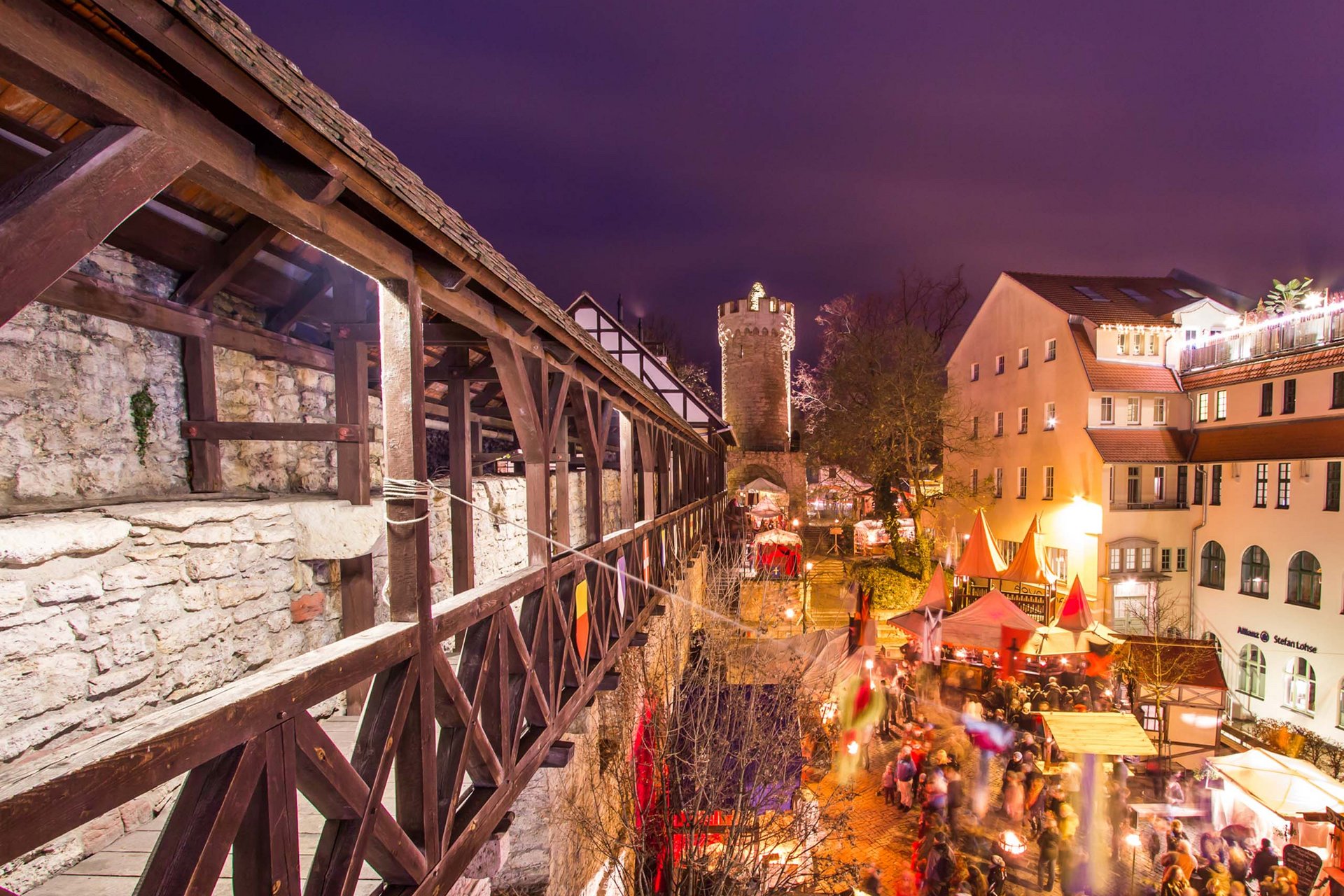 Mein Ferienresort in Thüringen Beleuchteter mittelalterlicher Markt mit Menschen neben alter Stadtmauer und Turm bei Nacht