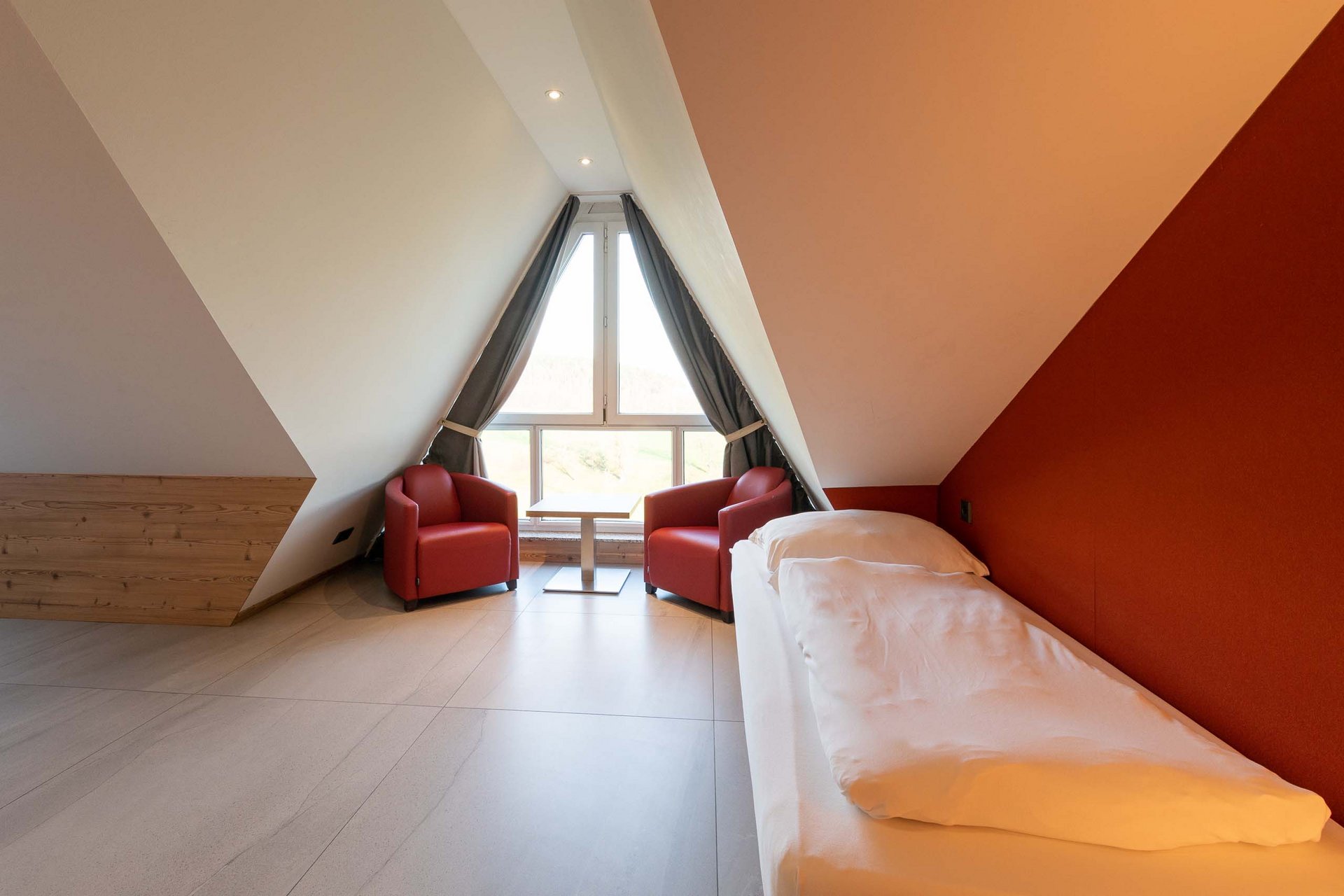 Vierbettzimmer Gemütliches Schlafzimmer mit zwei roten Sesseln und Einzelbett unter Dachschräge
