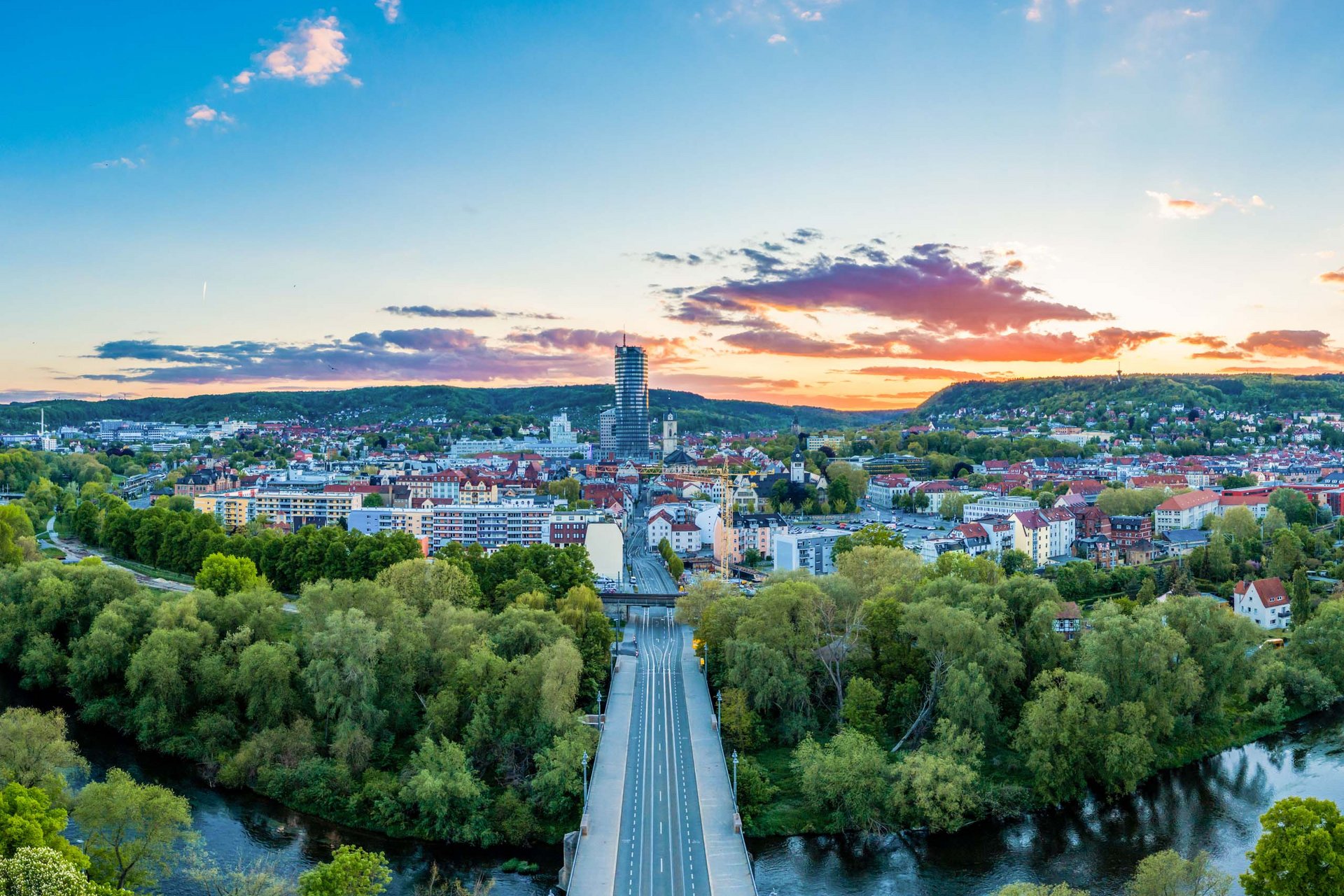 Wellnesshotel in Jena? Stadtansicht bei Sonnenuntergang mit Fluss, grünen Bäumen und Hochhaus