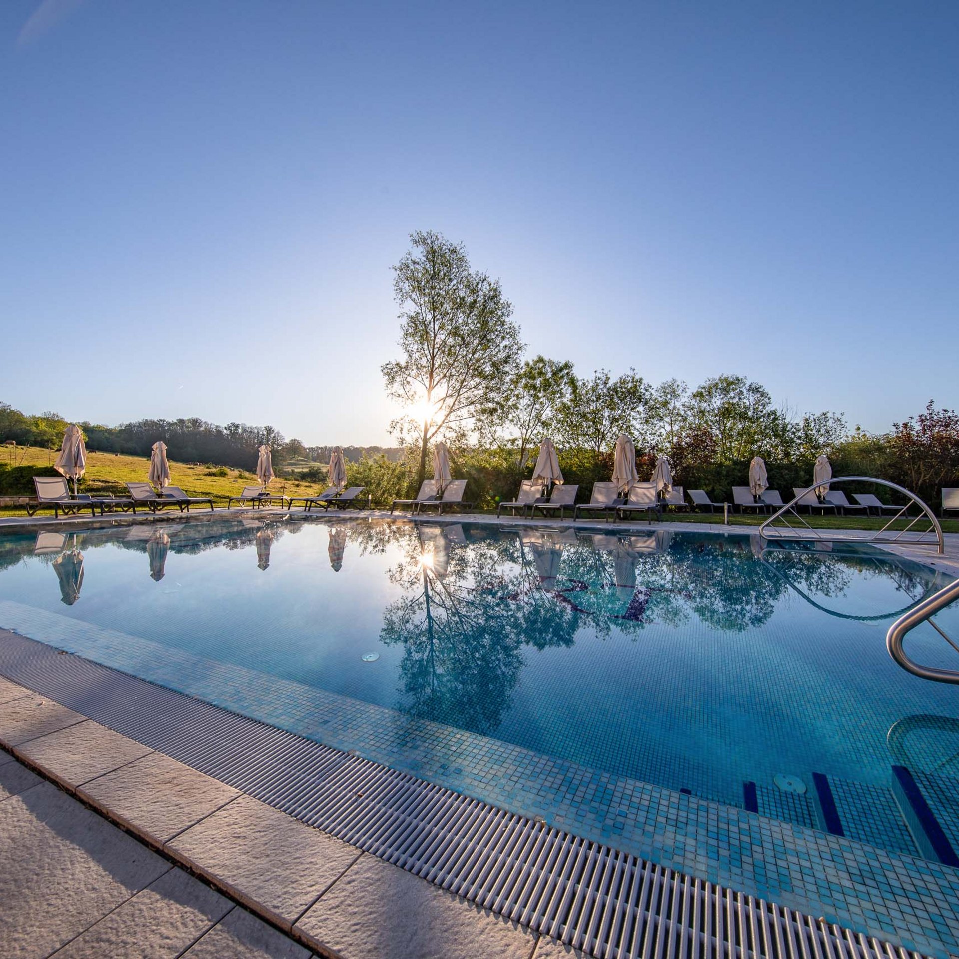 Urlaub in Jena: mein Fair Resort Ruhiger Außenpool mit Liegestühlen und Sonnenschirmen bei Sonnenuntergang