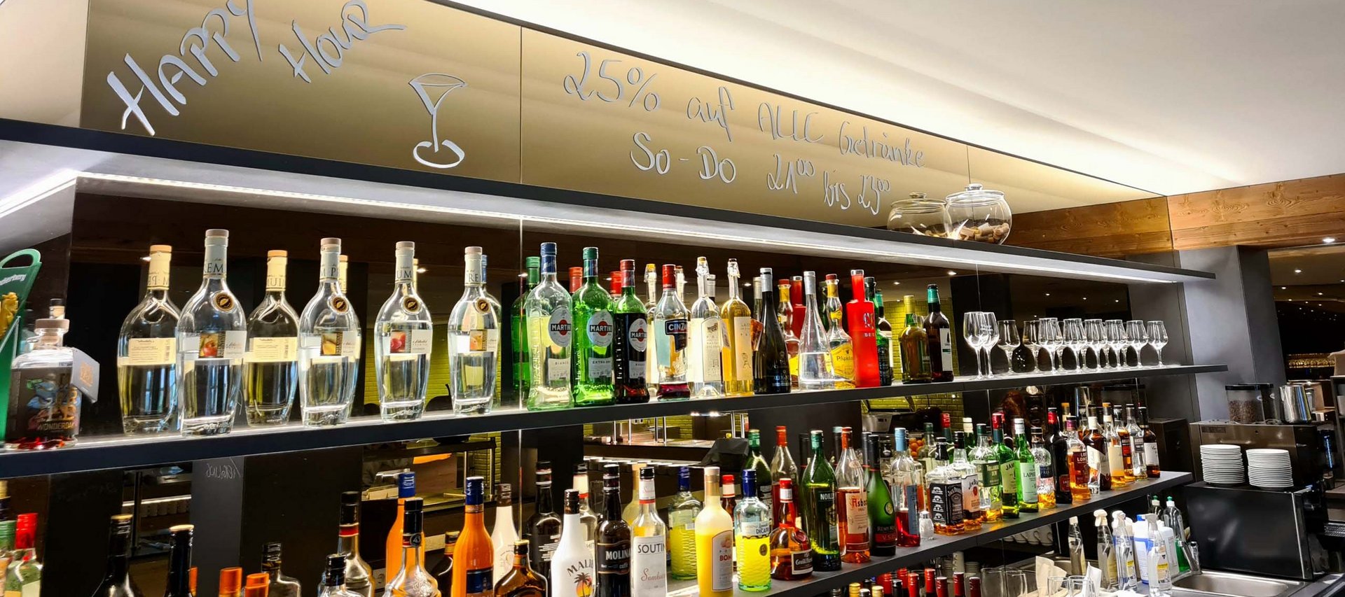 Ein Hotel in Jena mit All-inclusive-Verpflegung Barregal mit verschiedenen Alkoholflaschen und Happy Hour Angebot auf Spiegel geschrieben