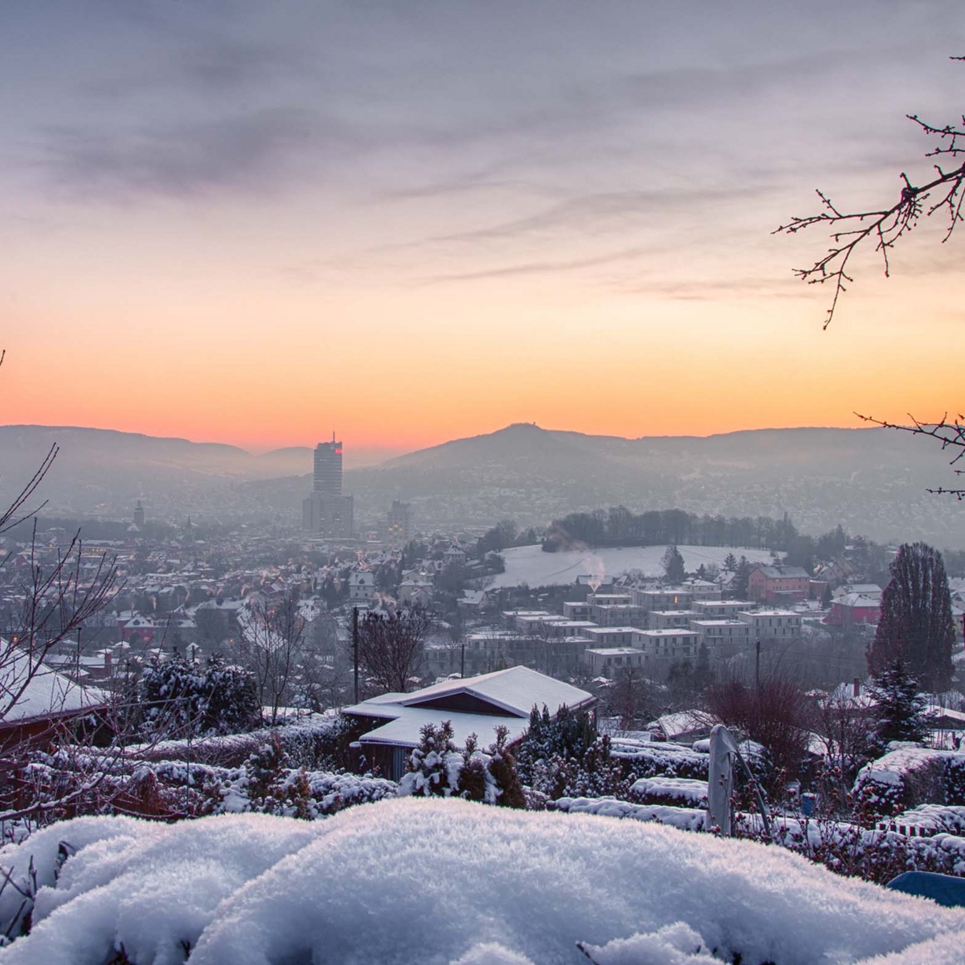 Sehenswürdigkeiten in und um Jena Schneebedeckte Häuser und Bäume bei Sonnenuntergang mit Bergen im Hintergrund