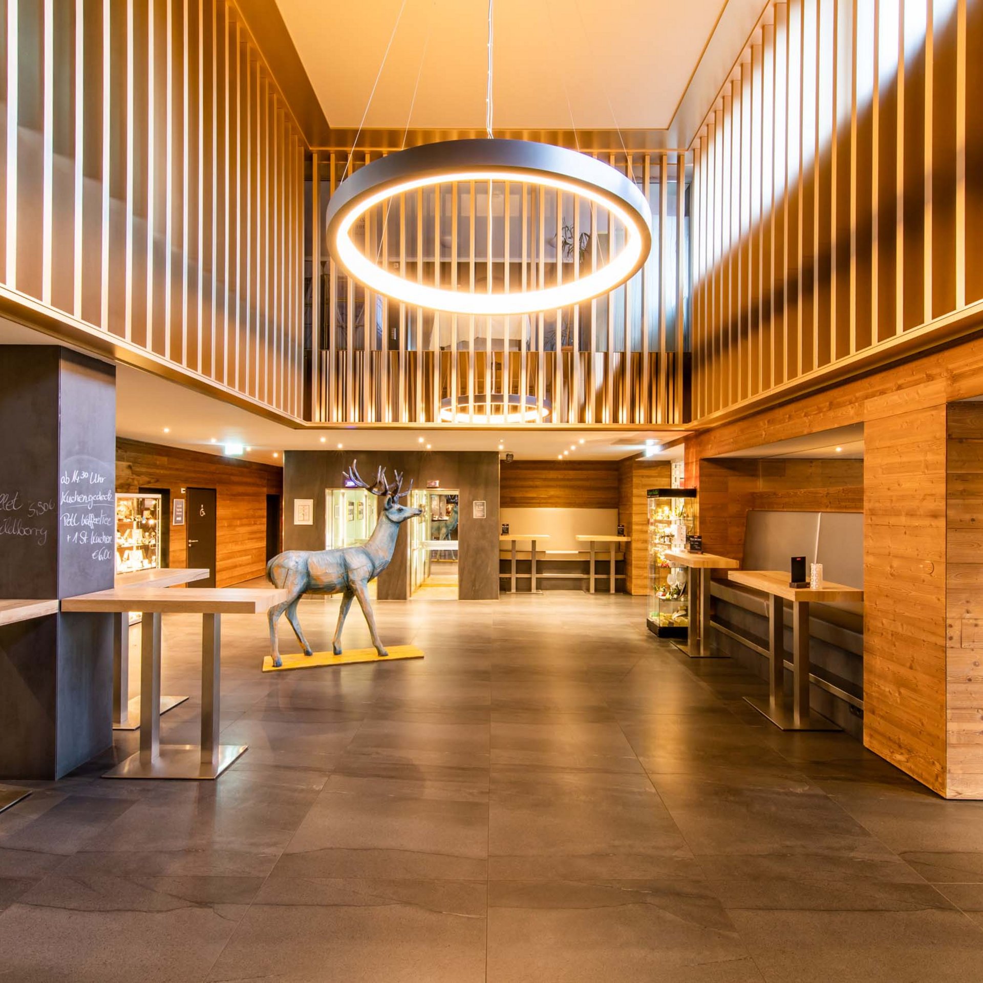 Urlaub in Jena: mein Fair Resort Helles Foyer mit Holzverkleidung, modernem Leuchtring und Hirsch-Dekoration