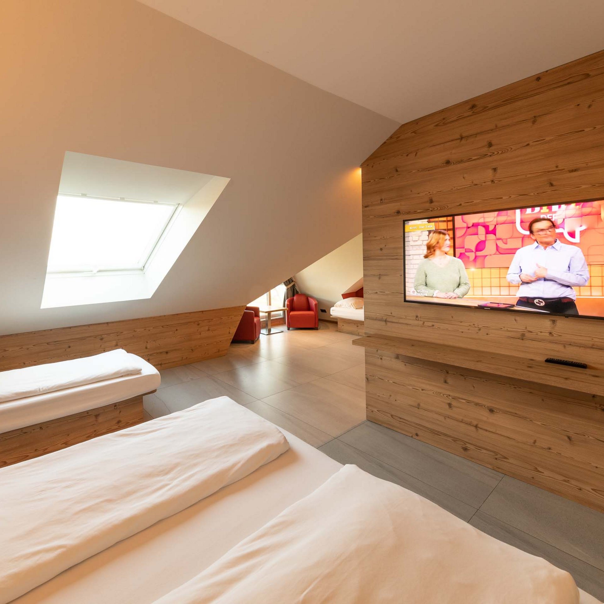 Vierbettzimmer Modernes Hotelzimmer mit zwei Betten, Dachfenster und Fernseher an Holzpaneelwand