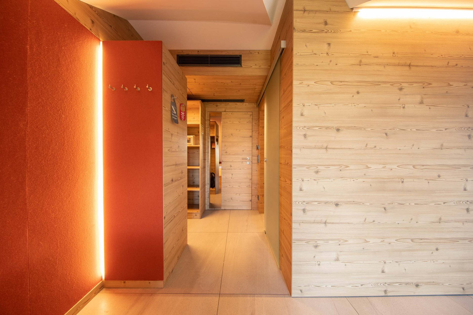 Vierbettzimmer Flur mit Holzverkleidung und orangefarbener Wand mit Beleuchtung und Haken