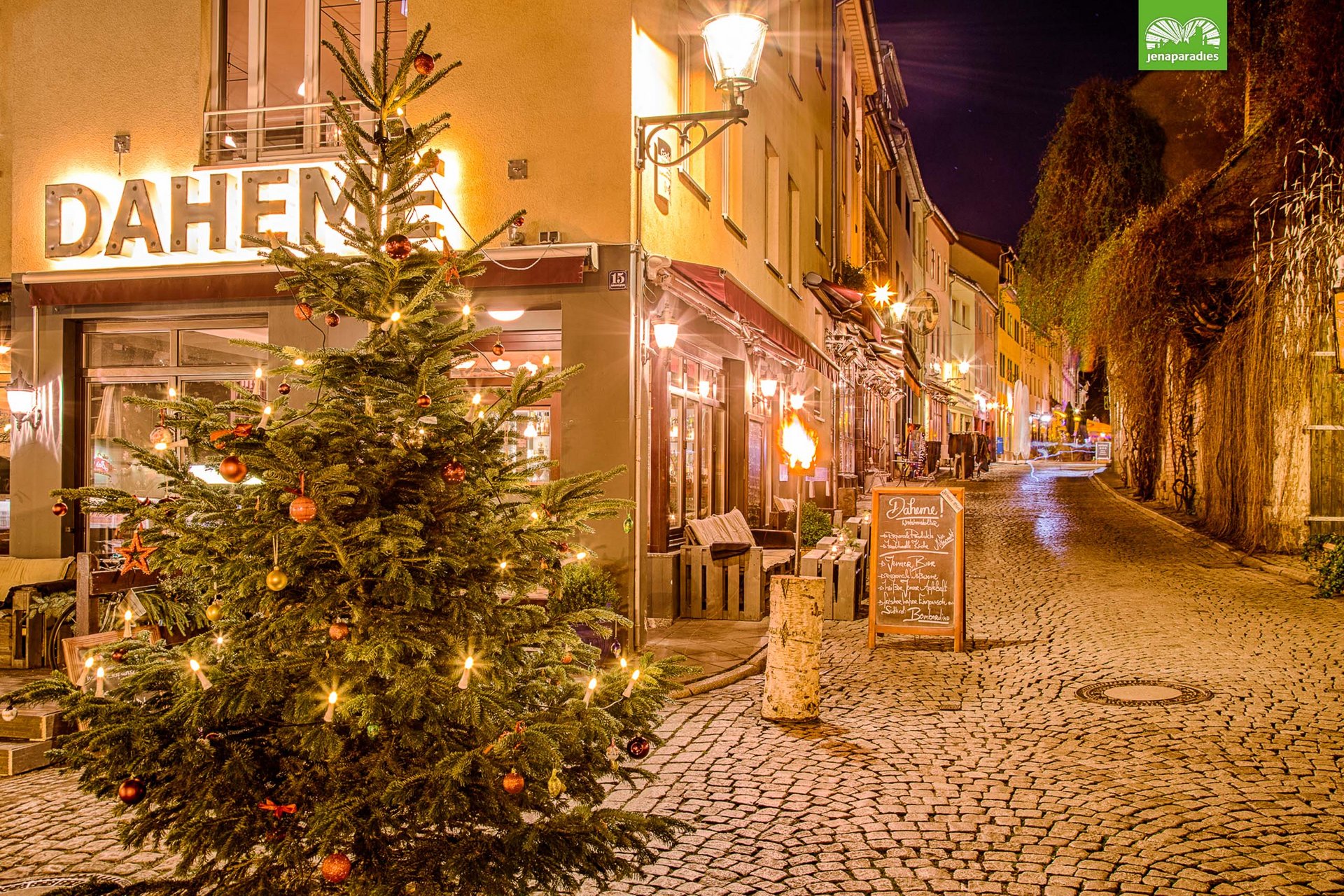Sehenswürdigkeiten in und um Jena Weihnachtsbaum vor beleuchtetem Restaurant Daheme in einer ruhigen Kopfsteinpflasterstraße bei Nacht