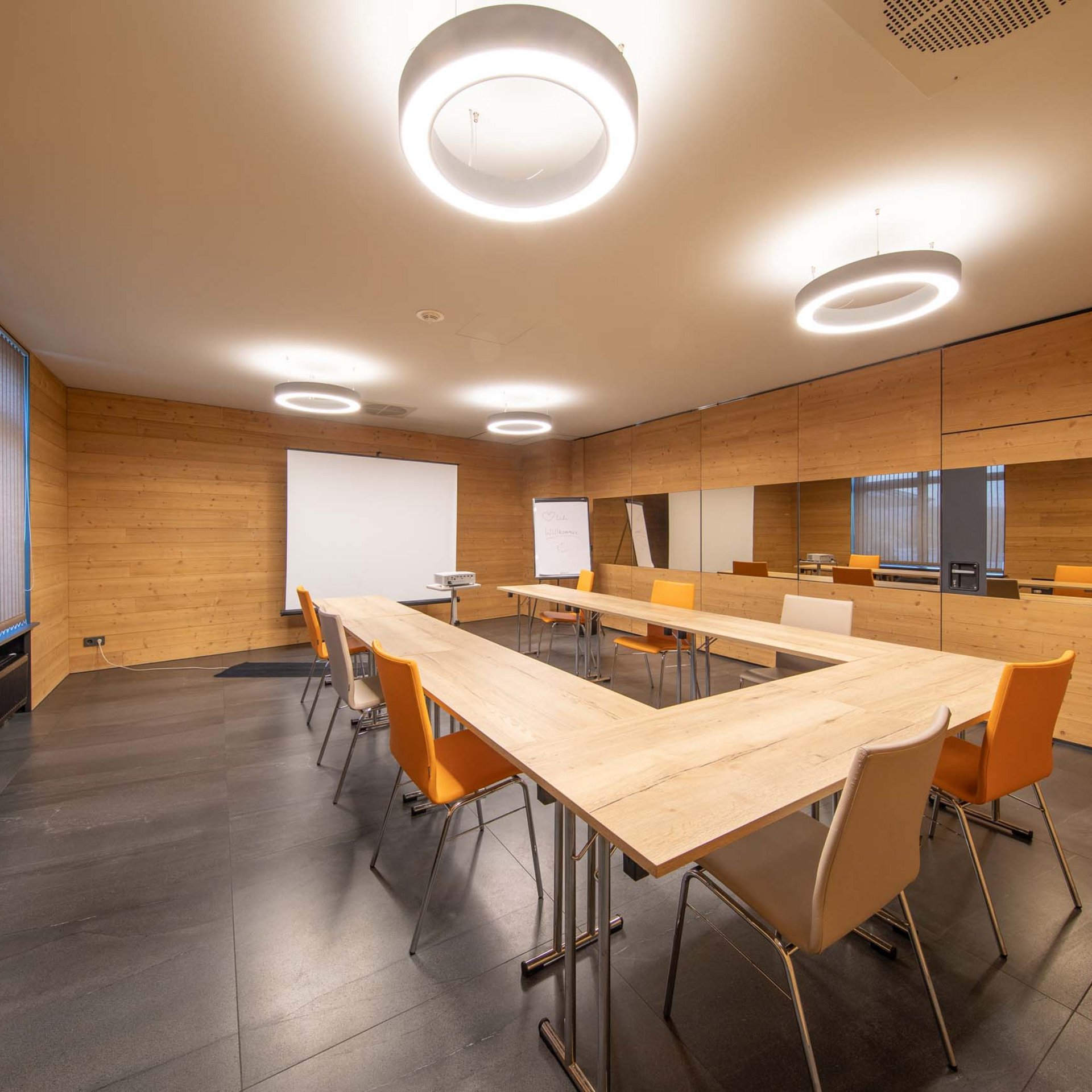 Das Event- und Tagungshotel in Jena Moderner Besprechungsraum mit Holzwänden, Tischen in U-Form und orangen Stühlen