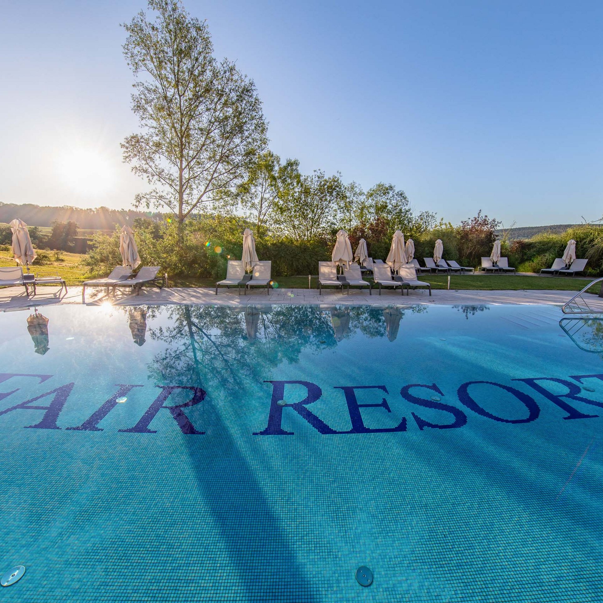 Das wohl beste Wellnesshotel in Thüringen Pool mit FAIR RESORT-Schrift im Wasser bei Sonnenuntergang und Liegestühlen